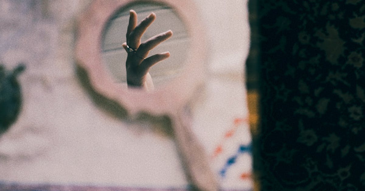 A hand reflected in a small rustic mirror on patterned fabric, creating a vintage artistic feel.